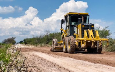 Yellow road grader leveling a dirt road in rural area on a sunny day.